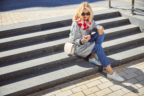 Smiling woman wearing blue jeans and grey coat spending time outdoors - Φωτογραφία, εικόνα