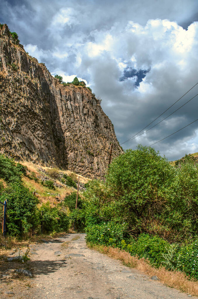 The darkened sky from the big storm clouds over the gorge Garni and the road passing about vertically standing basalt rocks and hills - Fotó, kép