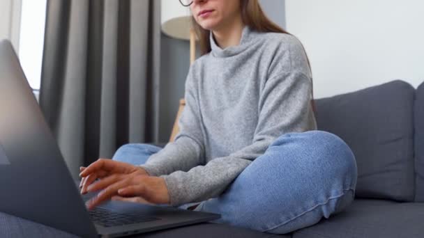 Nainen istuu mukavalla sohvalla ja työskentelee kannettavan tietokoneen kanssa. Etätyön käsite. - Materiaali, video