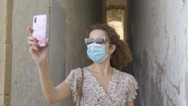 Gyönyörű göndör barna turista, sebészeti maszk vesz egy helyet a correlo de la rectoria Sitges, Spanyolország. - Felvétel, videó