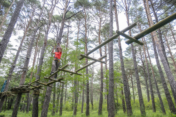 woman crossing a tibetan bridge in an adventure park in a pine forest horizontal - Photo, Image