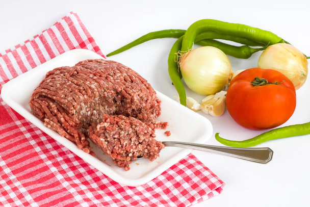 Főzetlen darált marhahús, fehér csomagolásban, kanállal és zöldséggel, széles kilátás - Fotó, kép