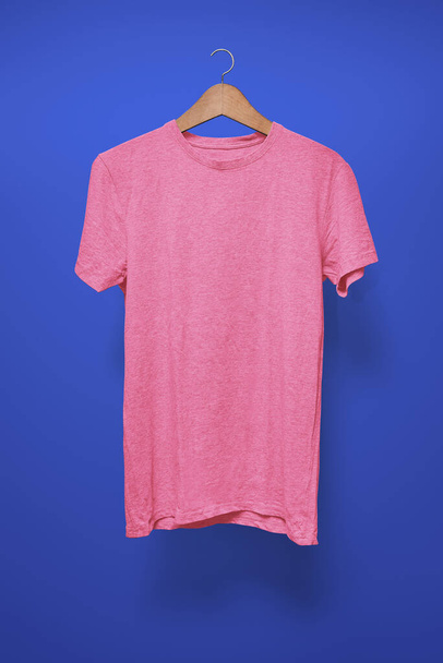 Vaaleanpunainen t-paita henkarissa tummansinistä taustaa vasten - Valokuva, kuva