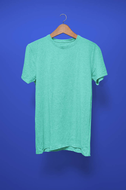 Turquoise T-Shirt op een hanger tegen een donkerblauwe achtergrond - Foto, afbeelding