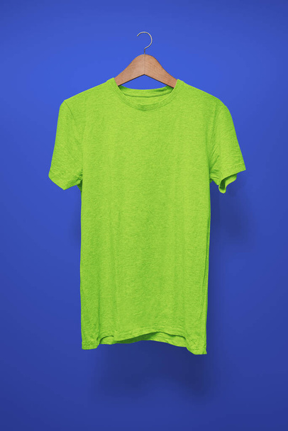 Grünes T-Shirt auf Kleiderbügel vor dunkelblauem Hintergrund - Foto, Bild