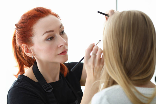 Stijlvolle make-up kunstenaar doet make-up op gezicht blond - Foto, afbeelding