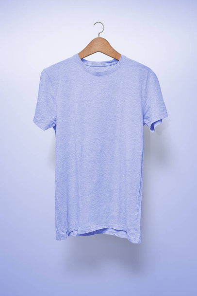 Hellblaues T-Shirt auf Kleiderbügel vor hellblauem Hintergrund - Foto, Bild
