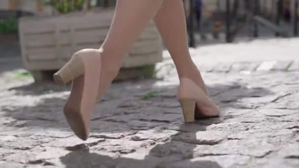 Camera follows feet of confident Caucasian woman in beige high-heels walking along pavement street on sunny day in city. Unrecognizable stylish lady strolling outdoors. Confidence, elegance, fashion. - Záběry, video