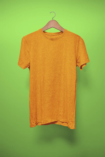 Помаранчевий T-Shirt на вішалці на зеленому тлі - Фото, зображення
