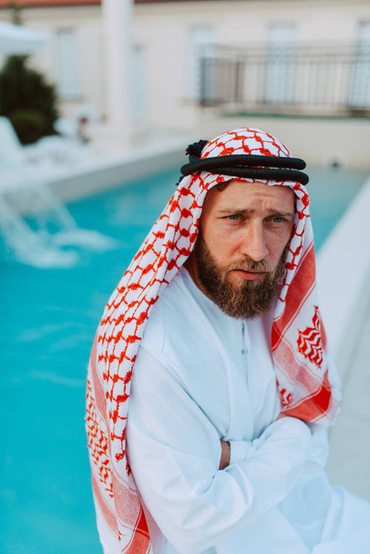 Porträt eines gutaussehenden muslimischen Mannes aus dem Nahen Osten in traditioneller Kleidung am Beckenrand sitzend - Foto, Bild