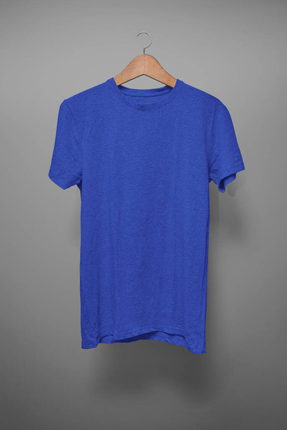Dunkelblaues T-Shirt auf Kleiderbügel vor grauem Hintergrund - Foto, Bild