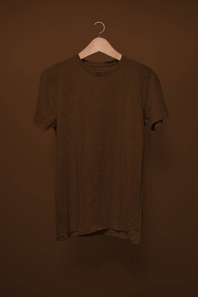 Braunes T-Shirt auf Kleiderbügel vor braunem Hintergrund - Foto, Bild