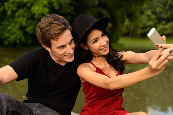 Portrait of young man and young Asian woman as multi ethnic couple together relaxing at the park outdoors - Photo, image
