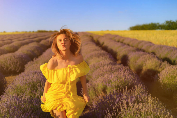 Happy young pretty smiling woman in a yellow dress dancing with happiness at sunset in a lavender field. The concept of joy and positive. Toned background. Lifestyle emotions - Фото, зображення
