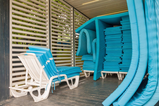 Ułożone białe leżaki lub leżaki z niebieskimi materacami na plaży drewniana altana lub baldachim słoneczny letni dzień. Zakończenie lub zerwanie koncepcji sezonu turystycznego - Zdjęcie, obraz