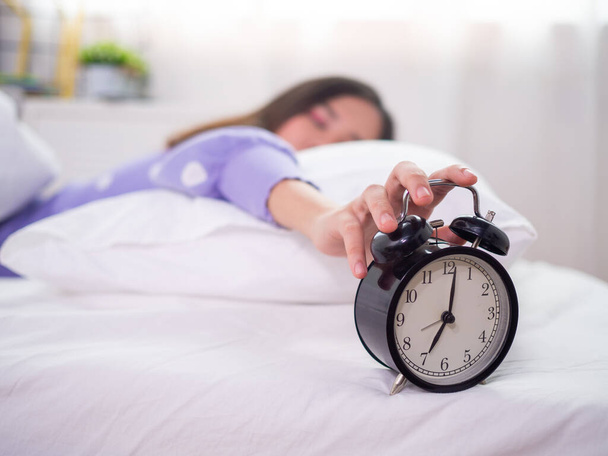 Сонна жінка спить у ліжку, використовуючи руку, щоб натиснути на будильник вранці. Доброго ранку в лінивий день
 - Фото, зображення