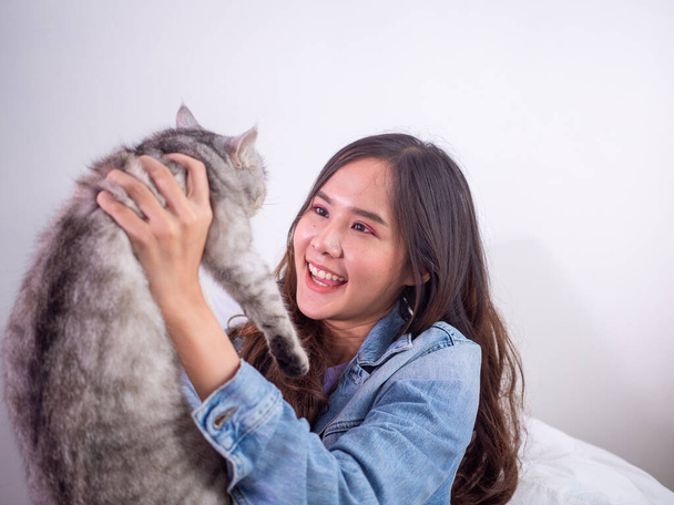 Длинноволосая женщина, играющая с серой кошкой, улыбающейся, поднимающей и дающей любовь домашним животным. - Фото, изображение
