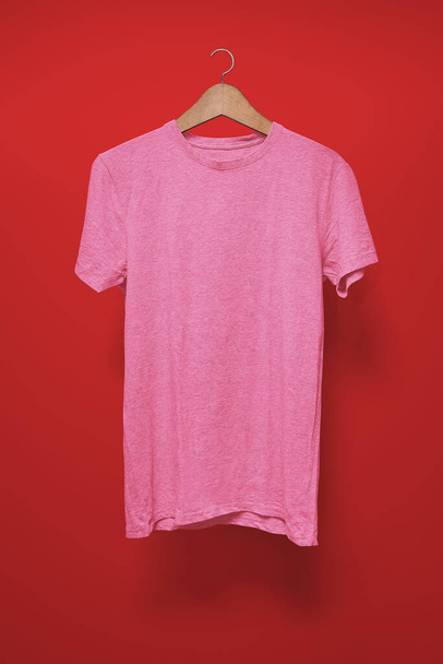 赤を背景にハンガーにピンクのTシャツ - 写真・画像