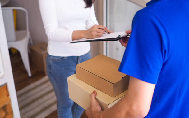 The woman is signing the name of the delivery staff sent to the front door. - Foto, Imagem