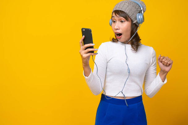 An Asian woman is holding a phone call and reading phone messages in shock and excitement. The bright yellow background. shock and wow concept - Foto, Imagen