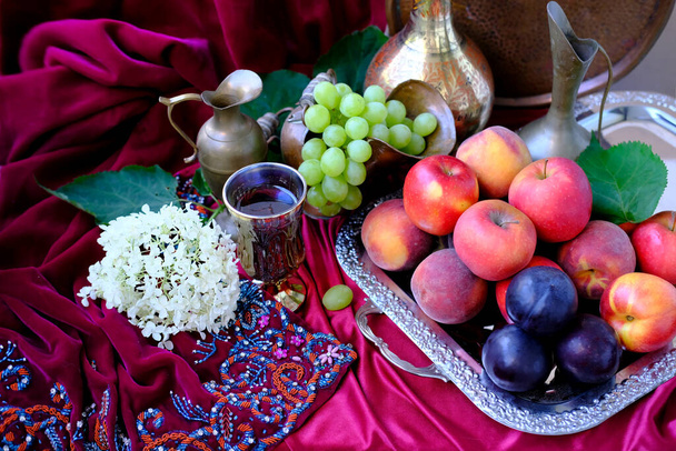 green grapes, plums, peaches, nectarines, jugs, a glass of wine, white hydrangea, a Dutch still life on a silk tablecloth, with velvet drapery, the concept of baroque - Fotografie, Obrázek