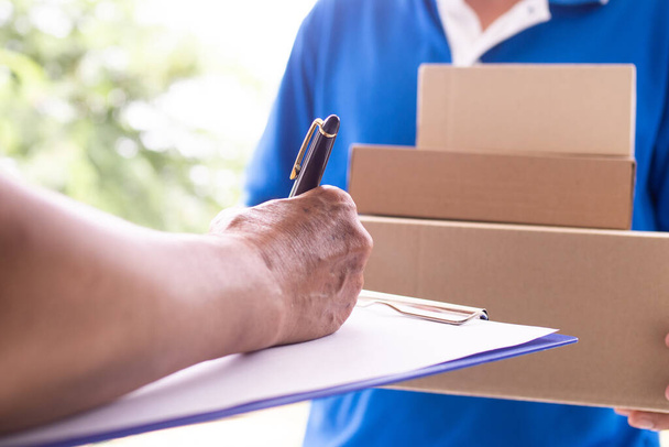 De hand van de huisbaas tekent om het pakje te ontvangen dat verstuurd wordt door de bezorger.. - Foto, afbeelding