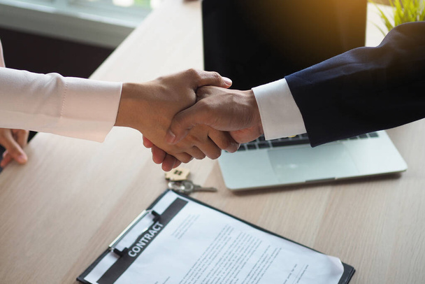 Zakenmensen en zakenvrouwen houden elkaars hand vast tijdens de bijeenkomst. Succesvolle deals over de handel in huis hebben beloofd papieren op de tafel. - Foto, afbeelding