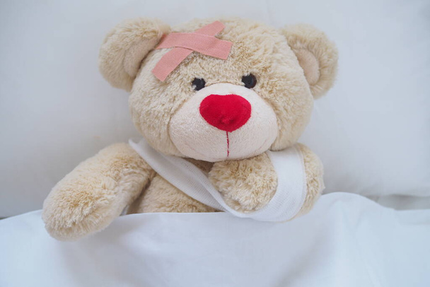 Teddy bear with a wound dress, wound and broken hands. Sleeping in bed. Sickness of children - Photo, Image