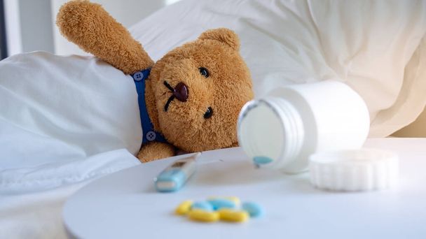 O urso de pelúcia triste teve uma dor de cabeça e febre, deitado doente na cama
. - Foto, Imagem