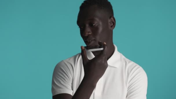 Giovane bello afroamericano uomo registrazione messaggio vocale su smartphone su sfondo colorato - Filmati, video