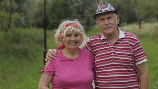 Senior caucasian couple walking in park embracing. Elderly man walks with woman. Husband, wife - Photo, Image