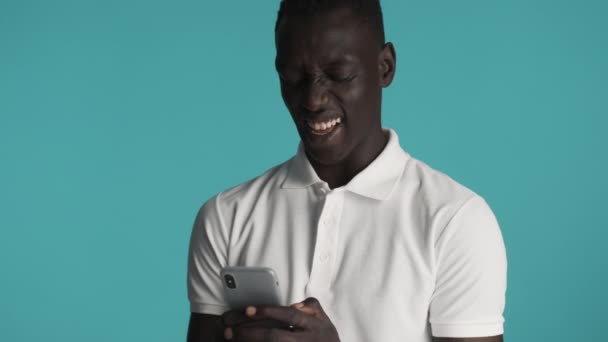 Atraktivní emoční Afroameričan chlap šťastně pomocí smartphonu a smích přes barevné pozadí - Záběry, video