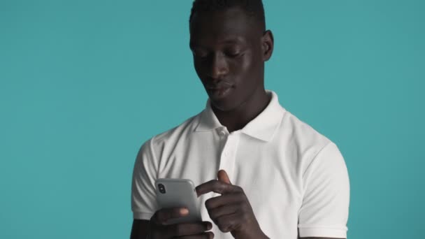 Atractivo chico afroamericano alegre felizmente usando teléfono inteligente sobre fondo colorido
 - Metraje, vídeo