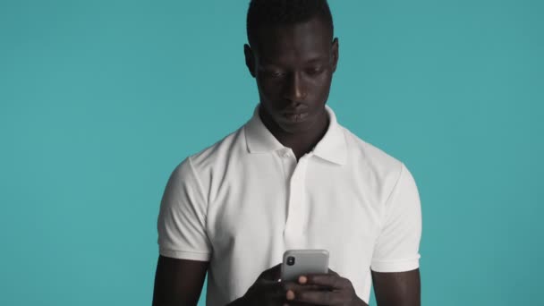 Aantrekkelijke stijlvolle Afro-Amerikaanse man met smartphone gelukkig kijkend in camera over kleurrijke achtergrond. Gezichtsuitdrukking - Video