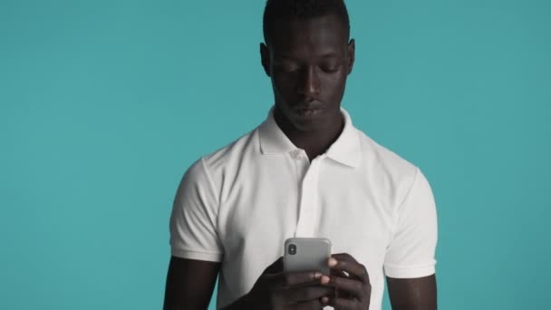 młody przystojny stylowy Afroamerykanin człowiek z zamiarem za pomocą smartfona w aparacie na kolorowe tło - Materiał filmowy, wideo