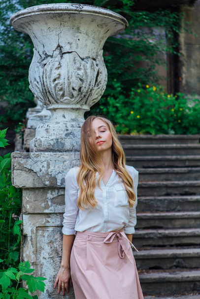 Portrait of a beautiful blond girl standing next to an old building with a decorative antique vase and stairs - Foto, immagini
