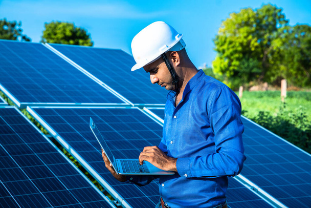 Engenheiro jovem trabalhando em laptop em pé perto de painéis solares, terra agrícola agrícola com fundo céu azul claro, energia renovável, energia limpa
. - Foto, Imagem