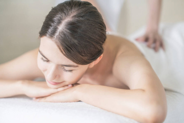 Genç bir kadın, parlak bir atmosferde güzellik salonunda masaj yaptırıyor. - Fotoğraf, Görsel