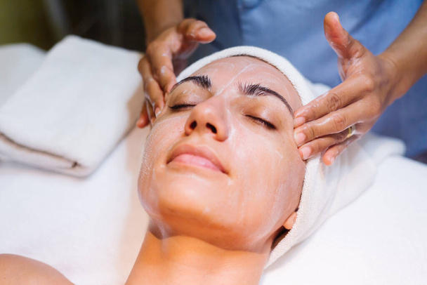Young woman lying on cosmetologist's table during rejuvenation procedure. Cosmetologist take care about neck and face skin youthfull and wellness. Hardware face cleaning procedure. - Photo, Image