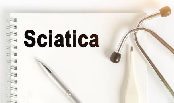 On the table are a stethoscope, a thermometer, a pen and a notebook with the inscription -Sciatica. The concept of medicine. - 写真・画像