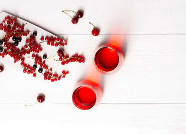 Twee glazen met vruchtensap gemaakt van rode bessen, kersen, zwarte bessen staan op een witte houten achtergrond, ernaast zijn bessen, bovenaanzicht, horizontale oriëntatie, er is een kopieerruimte. - Foto, afbeelding