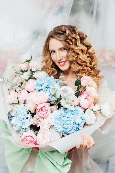 Όμορφο κορίτσι με όμορφο μακιγιάζ στο πρόσωπό της και χτένισμα με ένα μεγάλο πολυτελές μπουκέτο λουλούδια, διαφήμιση για κοσμητολόγους και ανθοπωλεία με διακοσμητές - Φωτογραφία, εικόνα