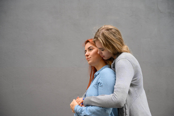 Two happy girlfriends are hugging on the background of a gray wall. Gentle hugs of a female lesbian couple. LGBT Same-sex marriage. - Foto, Imagem