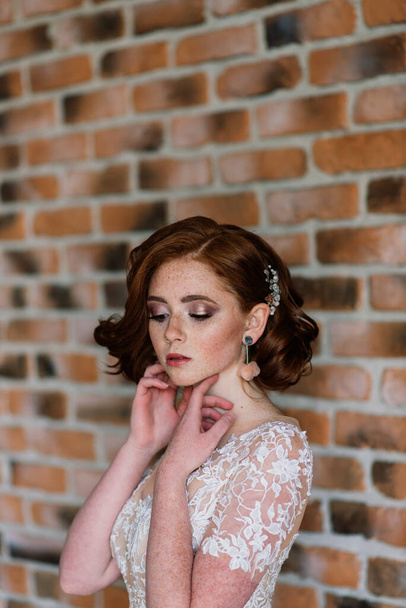 Porträt eines rothaarigen Mädchens im Hochzeitskleid vor weißgrauem Studiohintergrund. - Foto, Bild