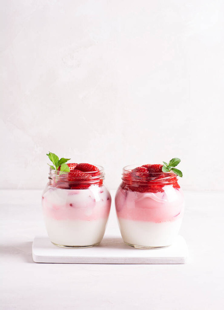 yogurt fatto in casa con fragole mature decorate con cavalletti di menta in banche su un cavalletto di legno su sfondo grigio.  - Foto, immagini