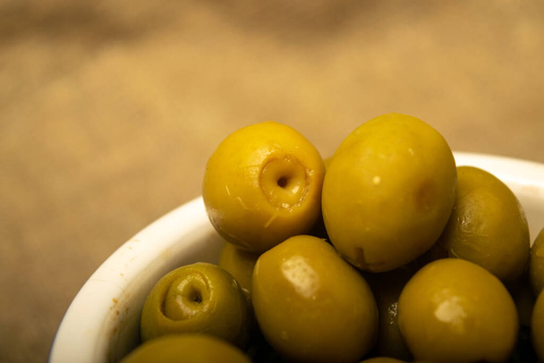 Vihreät oliivit keraamisessa kulhossa karkealla kuvioidulla säkkikangaspohjalla. Sulje se. - Valokuva, kuva