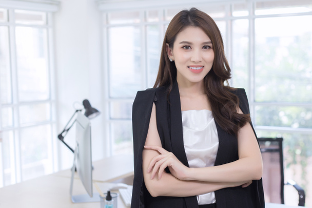 asiatique confiant femme est debout et bras croisé avec sourire visage dans salle de travail comme un fond. - Photo, image