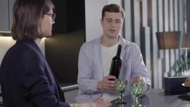 Portrait of cheerful young gay man opening bottle and pouring wine into glasses. Happy smiling Caucasian guy celebrating anniversary with boyfriend. Happiness, lgbt pride, diversity. - Záběry, video