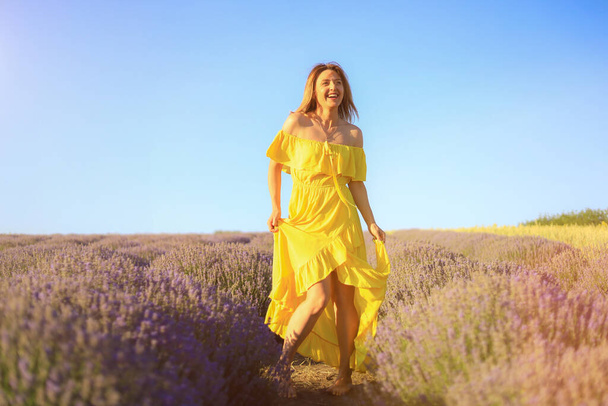 Szczęśliwa młoda, ładna, uśmiechnięta kobieta w żółtej sukience tańcząca ze szczęściem o zachodzie słońca na polu lawendy. Koncepcja radości i pozytywności. Uszkodzone tło. Emocje stylu życia - Zdjęcie, obraz