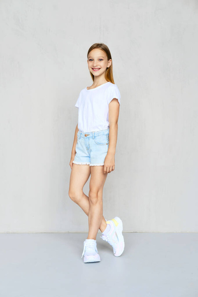 Young sportive girl in white t-shirt and jeans shorts posing in studio - Photo, image